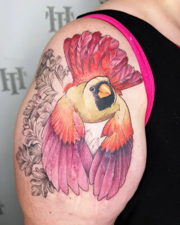 Colorful scar cover up tattoo on the upper arm featuring a vibrant cardinal with red, orange, and purple feathers, accented by soft black and grey floral elements in the background, expertly designed to cover up scars with bold, dynamic imagery.
