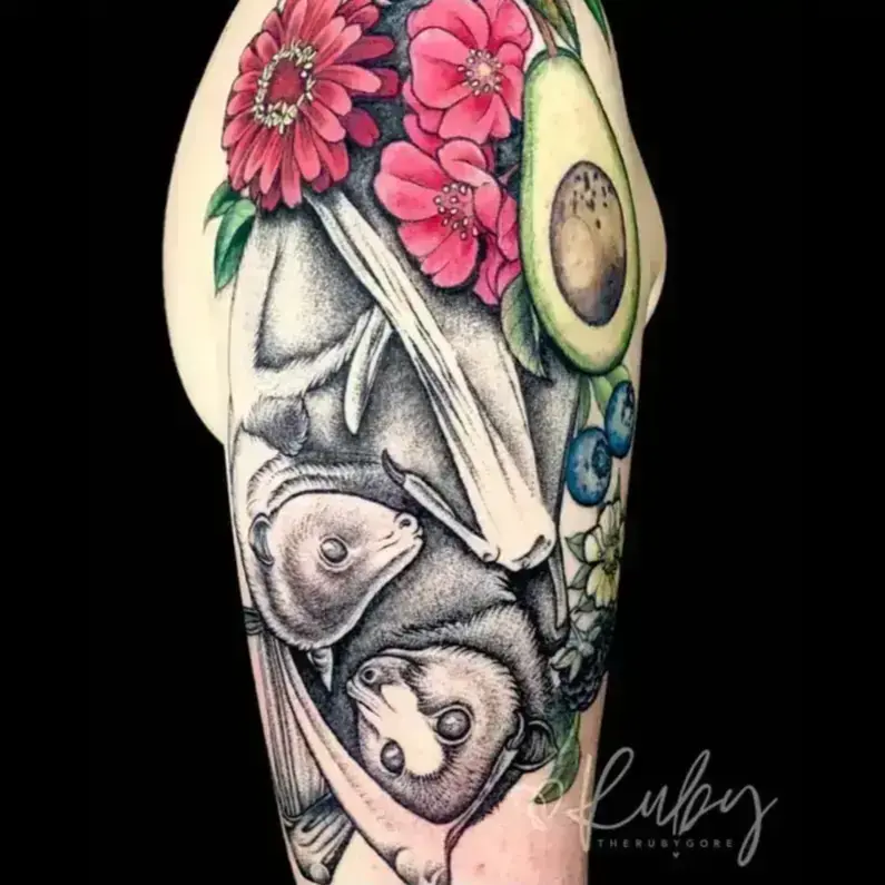Colorful fruit bat family tattoo on upper arm featuring vibrant colors and tropical fruits by botanical tattoo artist Portland Ruby Gore