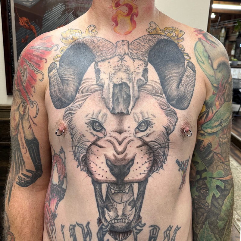 Black and grey lion head tattoo with ram skull on chest