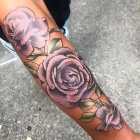 Colorful purple rose tattoo on forearm featuring realistic shading and green leaves by floral tattoo artist Ruby Gore in Portland