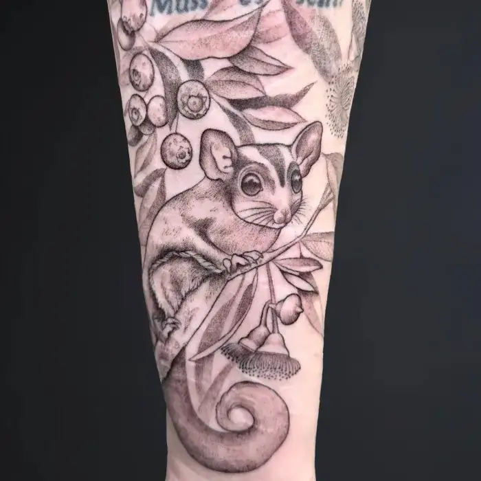 Detailed black and grey scar cover up tattoo on the forearm featuring a pet portrait tattoo of a realistic sugar glider surrounded by leaves and berries, symbolizing healing and personal growth. Ideal for those seeking tattoos for trauma or a meaningful trauma survivor tattoo.