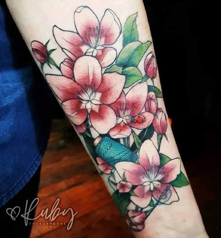 Colorful floral tattoo to hide scars on the forearm featuring pink blossoms, green leaves, and a ladybug, designed to effectively cover up self-harm scars.
