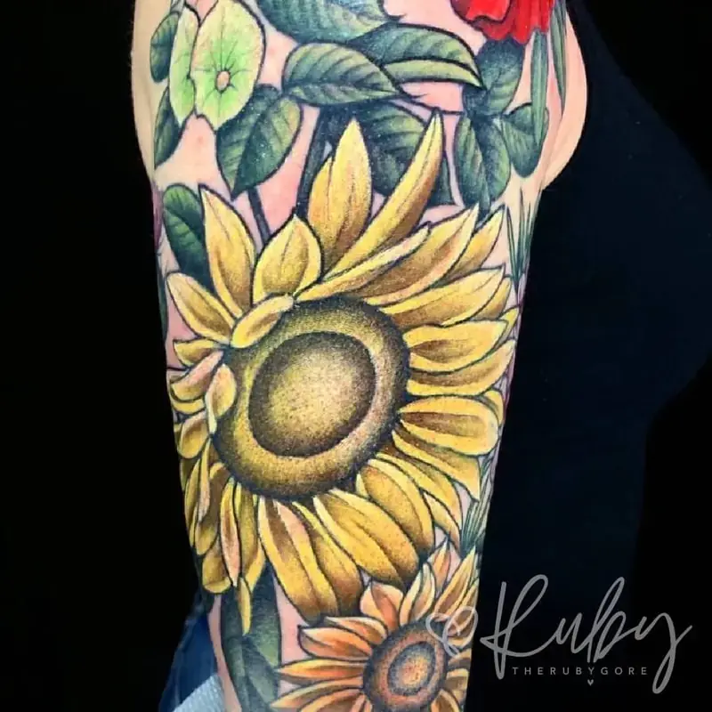 Large sunflower tattoo with vibrant yellow petals and green foliage tattoo on leg